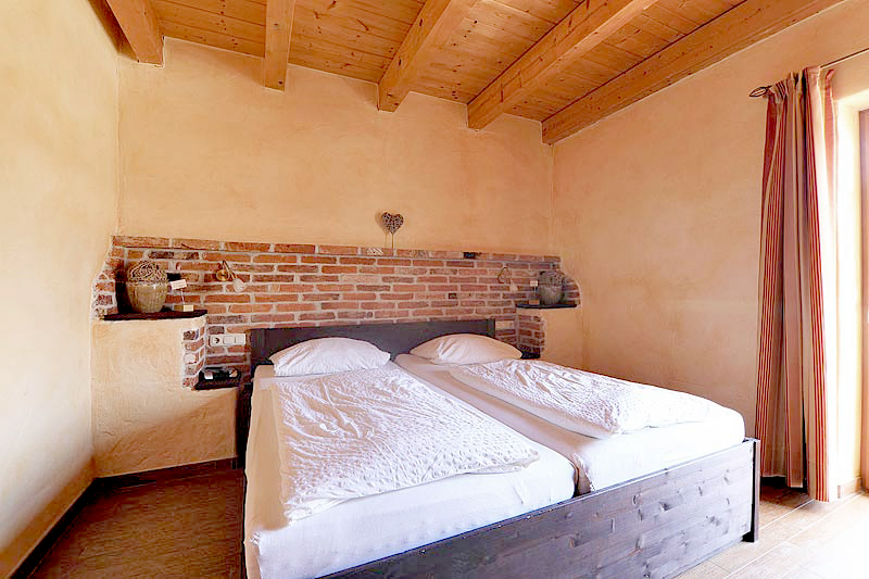 Schlafzimmer mit Dekosteinwand, Holzdekce, bezogenen Betten auf einen dunkelbrauen Bett