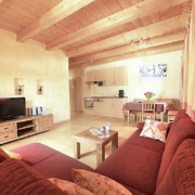 Ferienwohnung mit Holzdecke, Couch und TV, sowie Essecke und Kuechenzeile