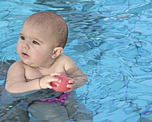 Baby im Schwimmbad mit Ball in der Hand