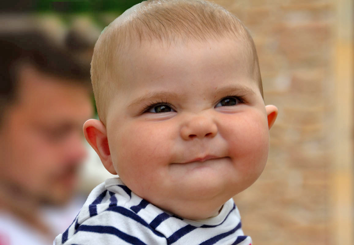 Baby lächelt mit Ringelshirt wenig Haares und dunklen Augen