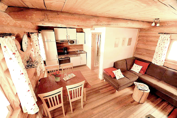 Blockhuette-Naturstammhaus mit Holzboden, Couch, Essecke und Küche, sowie Badezimmerbereich
