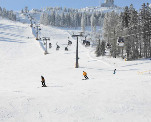 Skihang mit Kabinenlift mit verschneiten Bäumen, sowie einigen Skifahren