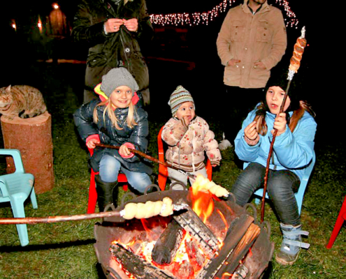 Kinder am lodernden Feuer mit Stockbrot und Würsetl