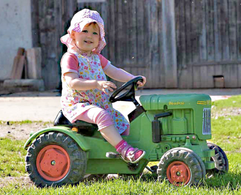 Kleinkind mit Sommerhut auf dem Trettraktor