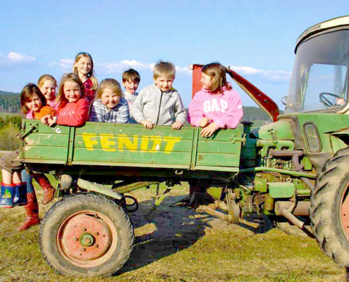 Acht Kinder sitzen auf einen Fendt Geräteträger auf einer Weise