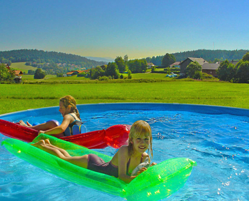 Inmitten schöner Landschaft spielen zwei Kinder auf der Luftmatraze im Pool