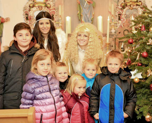 Christkind und Engel mit Kindern in einer Kapelle mit Weihnachtsbaum