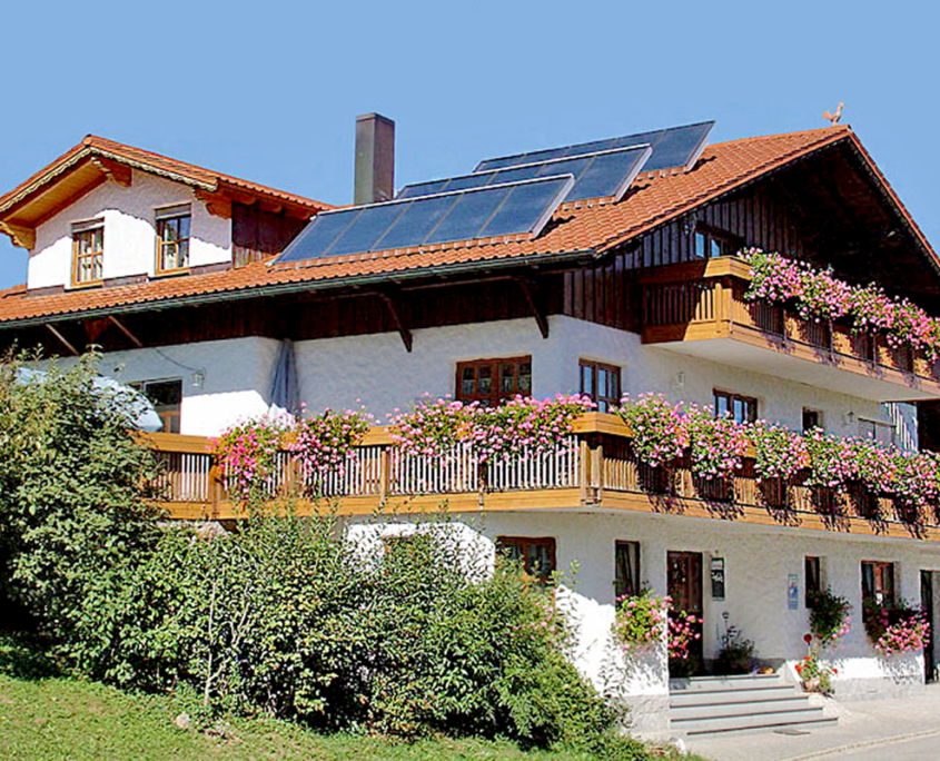 Ferienhaus mit großen Balkon, darauf viele Geranien und Sträucher um das Haus