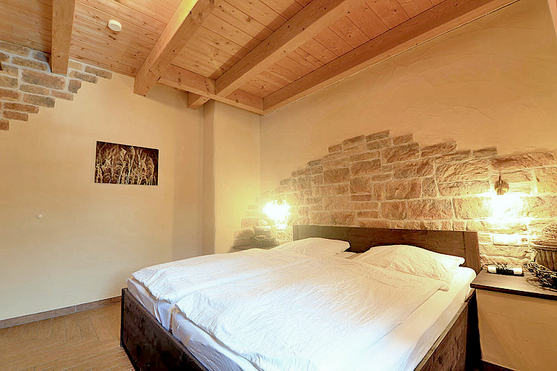 Schlafzimmer mit Holzdecke, brauen Holzbett und bezogenen Betten, dazu Wandleuchten und ein Foto an der Wand