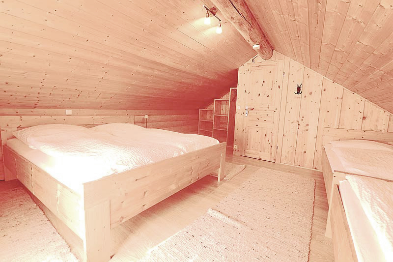 Schlafzimmer im Dachgeschoß mit vier großen Betten einem Regal und einer Tür, sowie Licht