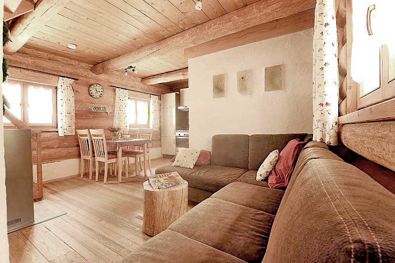 Wohnbereich in einem Chalet mit einem Rundstammtisch und Steinplatten an der Wand, sowie eine Essecke und eine Küche